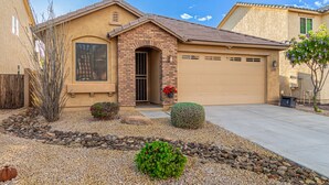 A single-story house with a garage, a small front porch, and a landscaped front yard with rocks and shrubs. - Bright 4BR Peoria Home | Heated Pool, Office, Desert Views (Sun City)