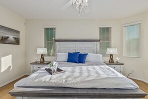 A bedroom with a large bed, two nightstands, a chandelier, and a painting on the wall.
