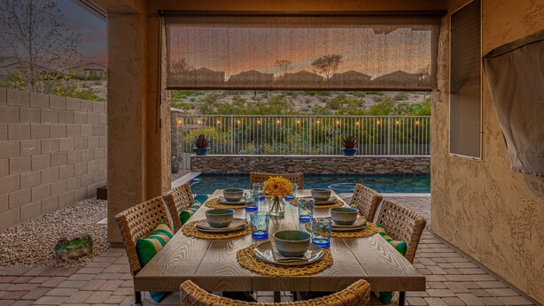 An outdoor dining area with a pool, wicker furniture, and a view of a desert landscape. - Bright 4BR Peoria Home | Heated Pool, Office, Desert Views (Sun City)