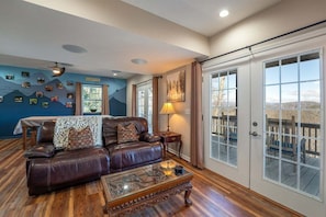 A living room with a leather sofa, a glass coffee table, and a view through a sliding door to an outdoor deck.