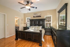 A bedroom with a dark wooden bed, a ceiling fan, a large mirror, and a window with a view.
