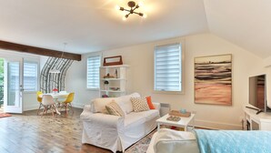 A spacious living area with a white sofa, a dining table with chairs, a TV, and a bookshelf. - Charming 2 bedroom rental unit in Knowlton village (Knowlton)