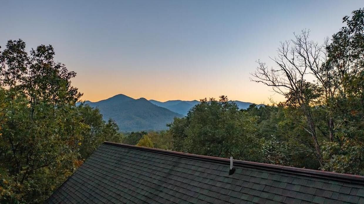 Une chaîne de montagnes au coucher du soleil, avec une maison au premier plan.