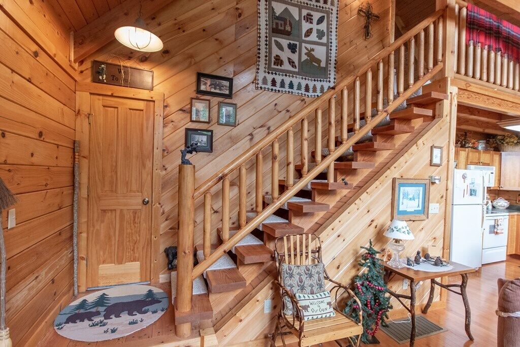 Interior de madera con una escalera, una puerta con la etiqueta “To” y una pequeña mesa con un árbol de Navidad.