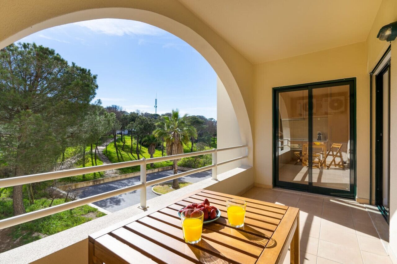 Un balcone con un tavolo di legno, due bicchieri di succo d'arancia e una ciotola di frutta.