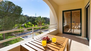 Een balkon met een houten tafel, twee sinaasappelsappen en een schaal fruit.