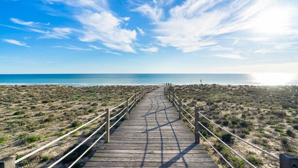 Een houten looppad dat naar een strand leidt, onder een heldere lucht.