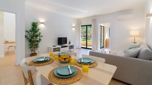 Een moderne woonkamer met een bank, een eettafel gedekt met borden en glazen, een televisie en een kamerplant.
