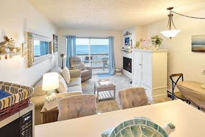 A living room with a sofa, armchairs, a coffee table, a fireplace, and a view of the ocean.