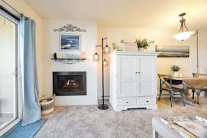 A living room with a fireplace, a dining table with chairs, a white cabinet, and a floor lamp.