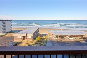 Vista de la playa con un estacionamiento, un edificio con puerta roja y una estructura de varios pisos al fondo.
