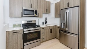 A modern kitchen with light wood cabinets, stainless steel appliances, and a white countertop.