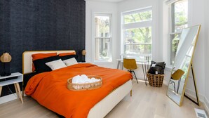 A modern bedroom with a large bed, a standing mirror, and a window with a view of trees.