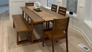 A dining room with a wooden table and chairs, a bench, and a decorative item on the table. There are two windows with blinds and a ceiling light fixture.
