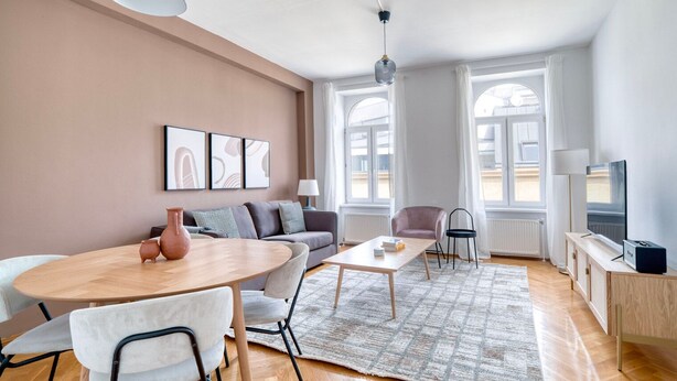 Una sala de estar moderna con un sofá, una mesa de comedor y un televisor. Hay ventanas amplias y una lámpara en el techo.
