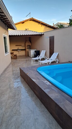 A swimming pool with two lounge chairs, a brick oven, and a tiled patio area. - A comfortable house in the center of Iguaba Grande with a pool. (Iguaba Grande)