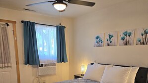 A bedroom with a bed, a ceiling fan, a window with curtains, and wall art.