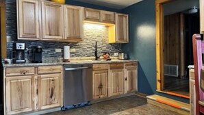 A kitchen with wooden cabinets, a dishwasher, and a stone backsplash. - Coyote - Upper Canyon w Priv Hot Tub, Big Decks, Wood Fireplace (Ruidoso)