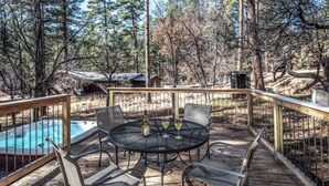A wooden deck with a hot tub, a round table with chairs, and a pool. - Coyote - Upper Canyon w Priv Hot Tub, Big Decks, Wood Fireplace (Ruidoso)