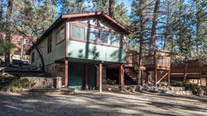 A two-story building with a green and red exterior, a covered porch, and a wooden deck. - Coyote - Upper Canyon w Priv Hot Tub, Big Decks, Wood Fireplace (Ruidoso)