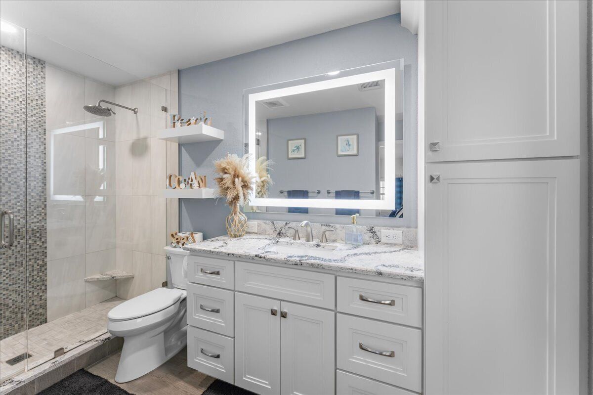 Une salle de bain moderne avec une douche à parois de verre, des toilettes blanches, un meuble-lavabo avec un grand miroir et un évier.