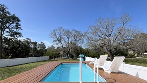Une piscine rectangulaire dotée d’une terrasse en bois, entourée de rampes blanches et de chaises longues.