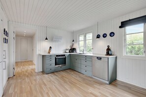 A kitchen with white wooden walls, a wooden floor, a built-in oven, a sink, and a dishwasher. - Lovely cottage for family and friends (Kirke Hyllinge)