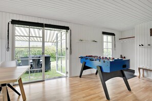 A room with a foosball table, a table with chairs, and a view through a glass door to an outdoor patio. - Lovely cottage for family and friends (Kirke Hyllinge)