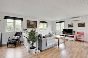 A spacious living room with a sofa, a chair, a TV, and a dining table. - Lovely cottage for family and friends (Kirke Hyllinge)