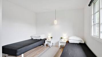 Een kamer met twee bedden, een klein wit nachtkastje met een lamp, een hanglamp en een raam.
