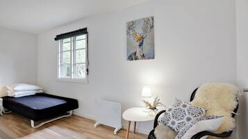 Quarto com cama, radiador, cadeira, mesa com abajur e janela.