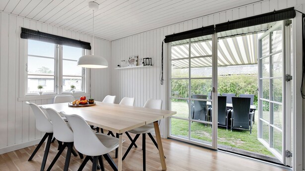 A dining area with a wooden table, white chairs, and a large window with a view of the outdoors.