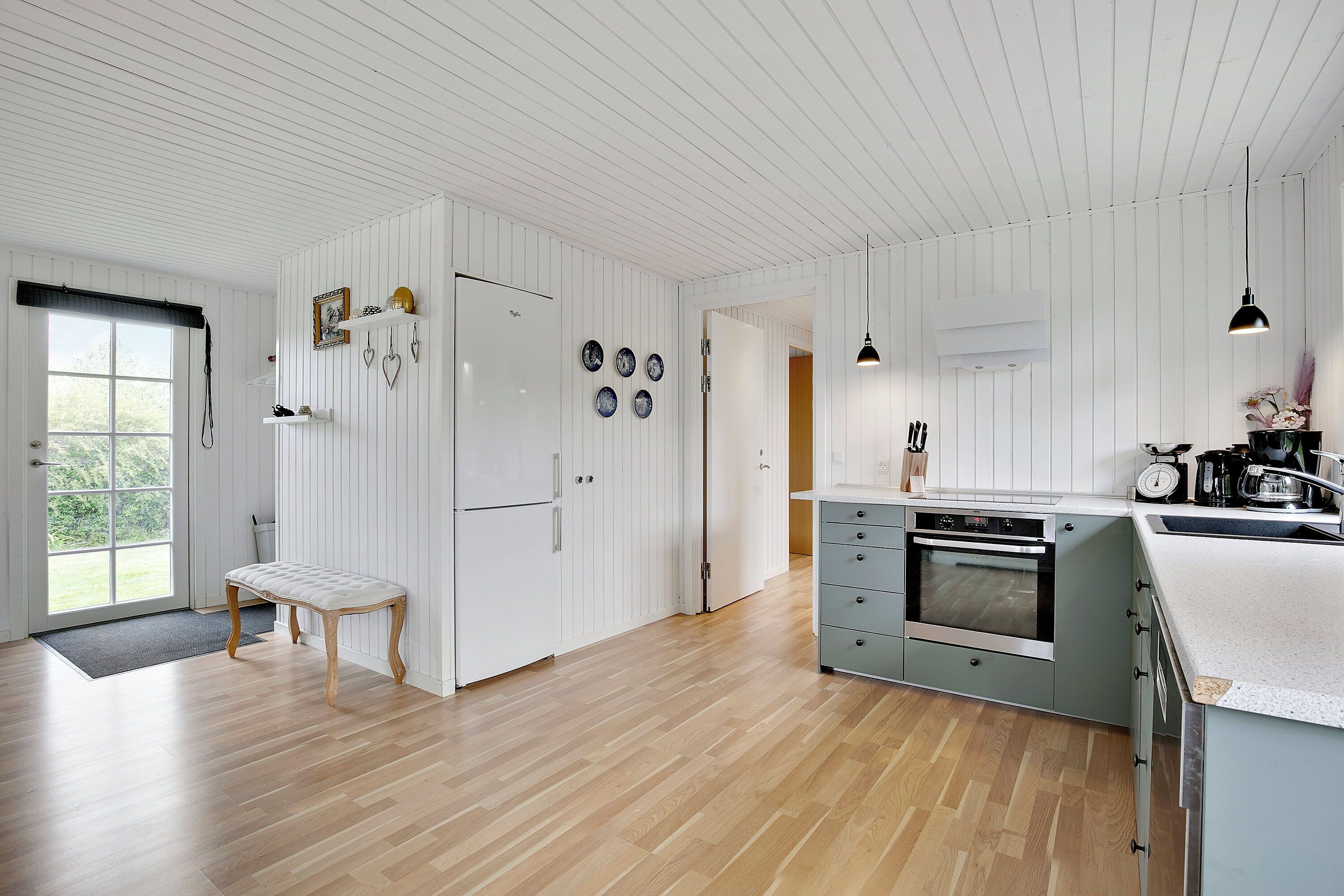 Een moderne keuken met witte kasten, een houten bankje en een groot eiland met een spoelbak.
