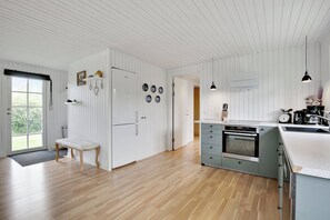 A modern kitchen with white cabinetry, a wooden bench, and a large island with a sink. - Lovely cottage for family and friends (Kirke Hyllinge)