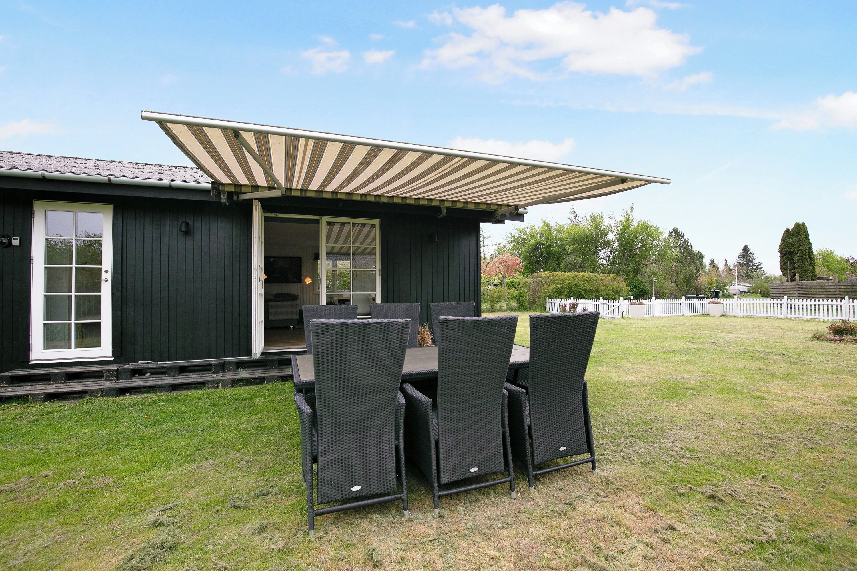 Une maison avec une table et des chaises sur une terrasse, une porte coulissante et, au fond, une clôture blanche.