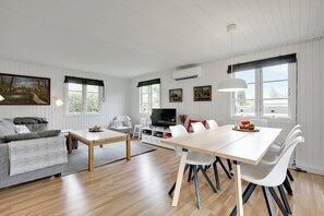 A modern living room with a sofa, coffee table, dining table, and chairs. - Lovely cottage for family and friends (Kirke Hyllinge)