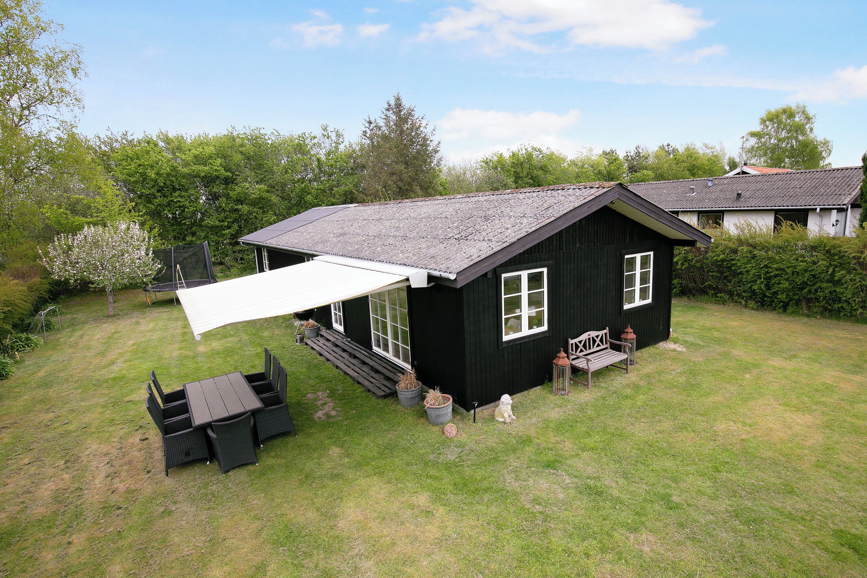 A black house with a white awning, a patio table, and a small garden area.