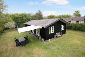 Ein schwarzes Haus mit einer weißen Markise, einem Patio-Tisch und einem kleinen Garten.