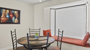 A dining area with a round table, four chairs, a potted plant, and a window with blinds. - Sandestin Beachside II Oasis (Miramar Beach)