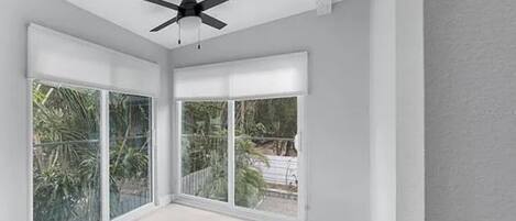 A spacious room with large sliding glass doors, a ceiling fan, and a view of greenery outside.