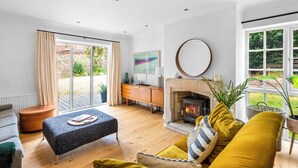 A modern living room with a fireplace, a sofa, a coffee table, and a view of the garden through large windows. - Stunning 3-Bed House in Saffron Walden (Saffron Walden)
