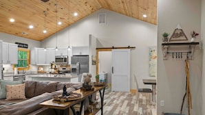 A spacious living area with a high ceiling, wooden beams, a brown leather sofa, and a dining table with decorative items.