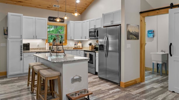 A modern kitchen with white cabinets, a stainless steel refrigerator, and a wooden ceiling.