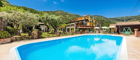 A swimming pool with a house in the background, surrounded by greenery and hills.