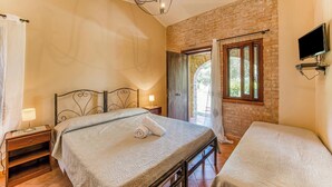 A bedroom with a bed, bedside table, lamp, and a TV mounted on the wall. - Local Stone Cottage With Shared Pool, Casal Velino, Italy (Casal Velino)
