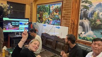 A wooden interior with a television displaying a news channel, a painting of a waterfall, and a group of people seated.