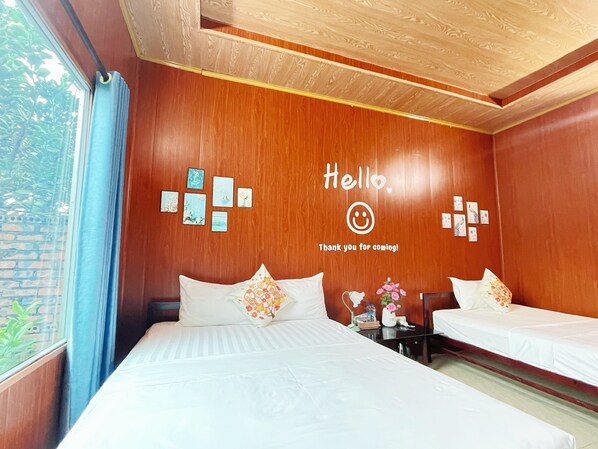 A hotel room with two beds, wooden walls, a 'Hello' sign, and a window with curtains.