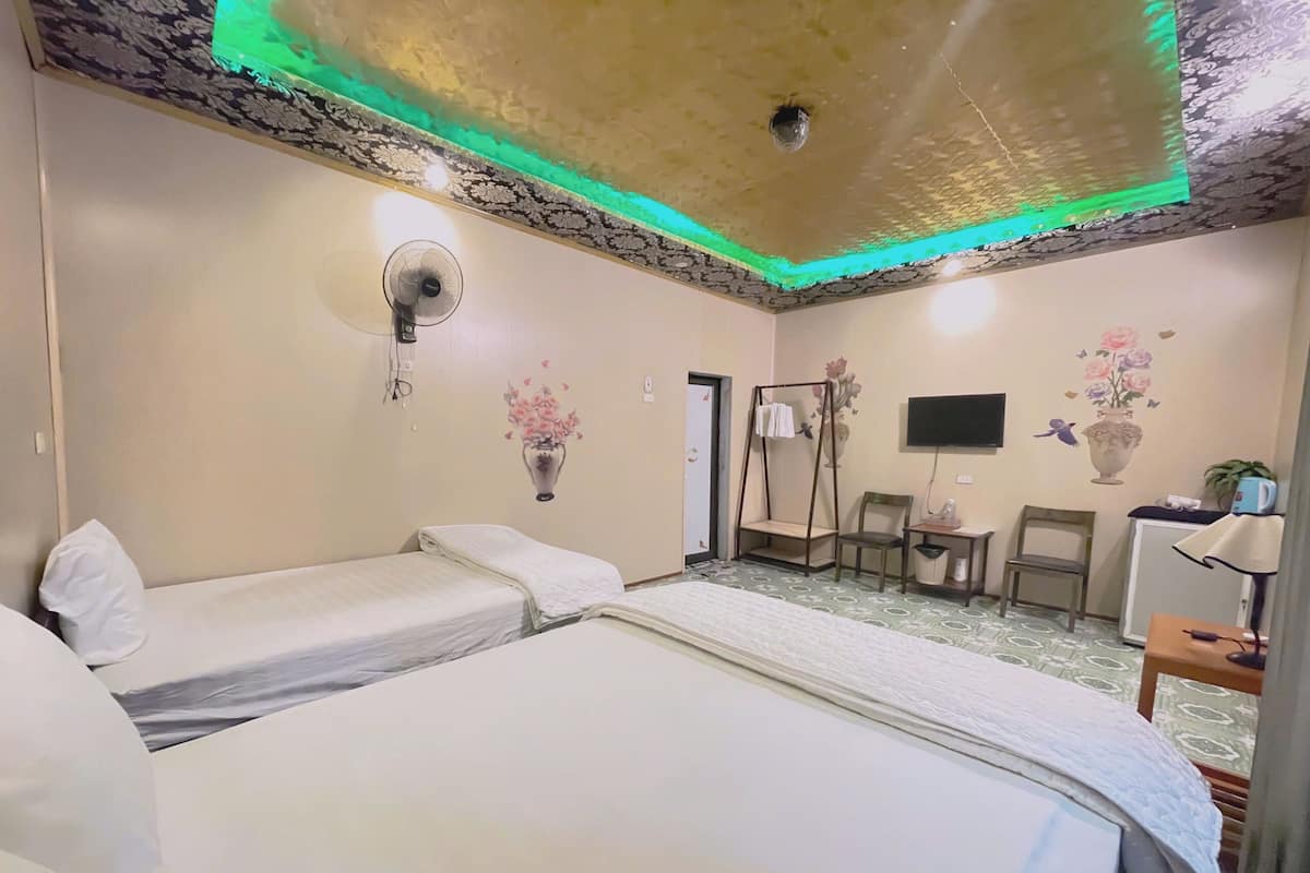 Habitación de hotel con dos camas individuales, un escritorio con silla, un televisor y una pequeña mesa con una silla.