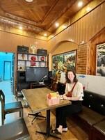 Una mujer sentada a una mesa en una habitación con paneles de madera, un televisor y un cuadro en la pared.