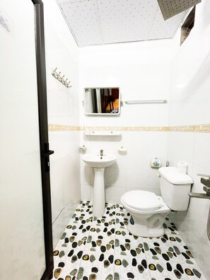 Un baño con lavamanos, inodoro y espejo blancos. El piso tiene un diseño de baldosas con motivos.